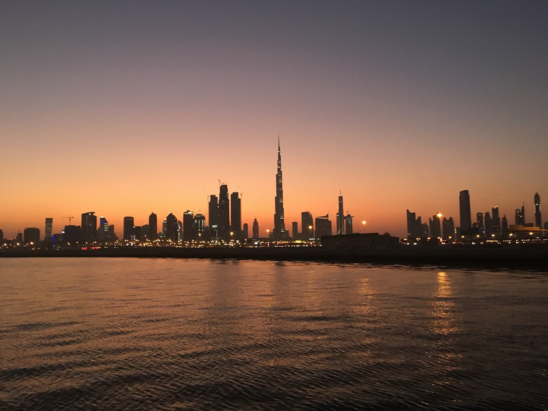 The Burj Khalifa's illuminated spire towering over Dubai's skyline at dusk, seen across the water