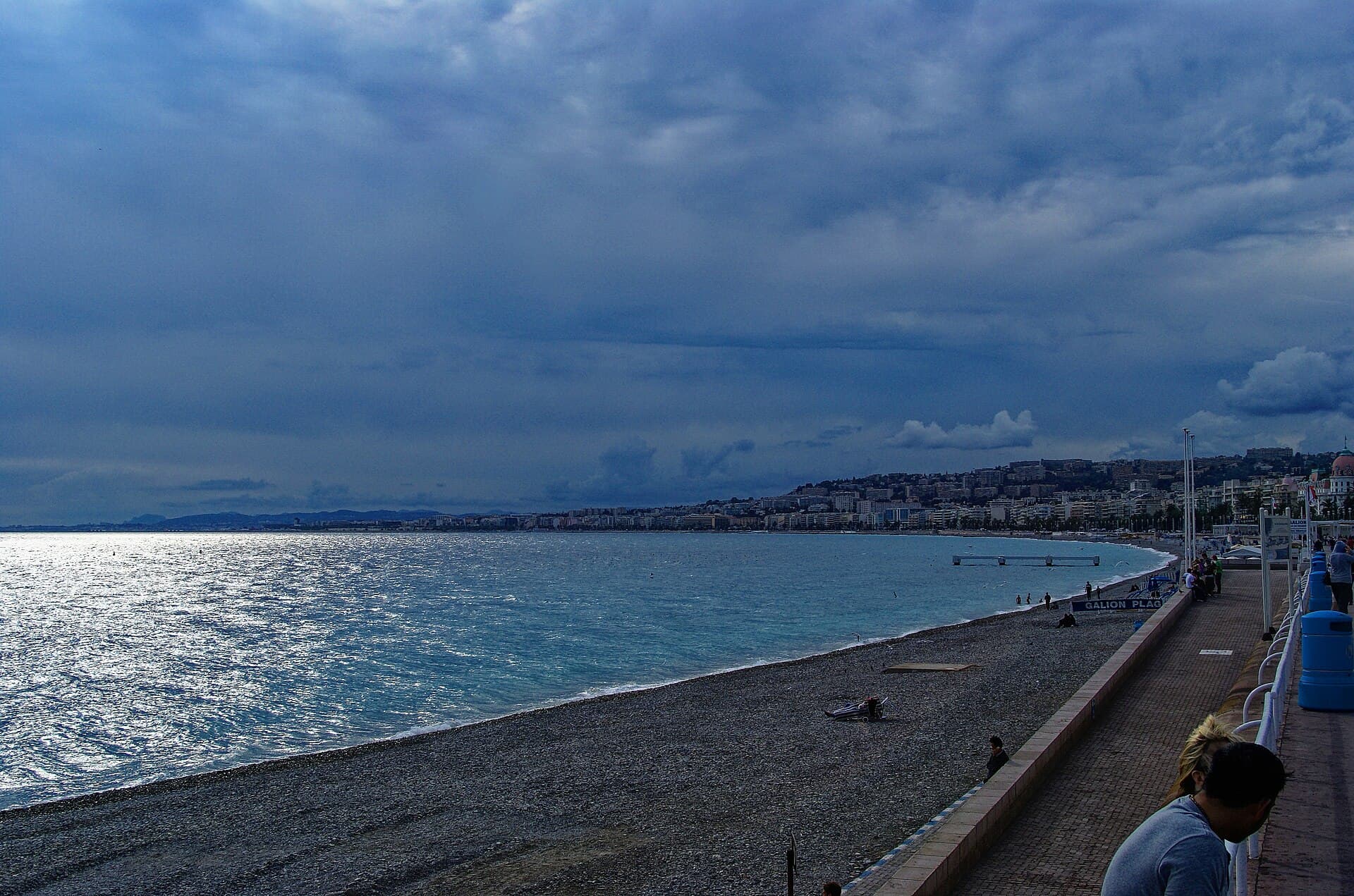 The pebble beach and curving seafront of the Promenade des Anglais in Nice, with the city stretching along the bay