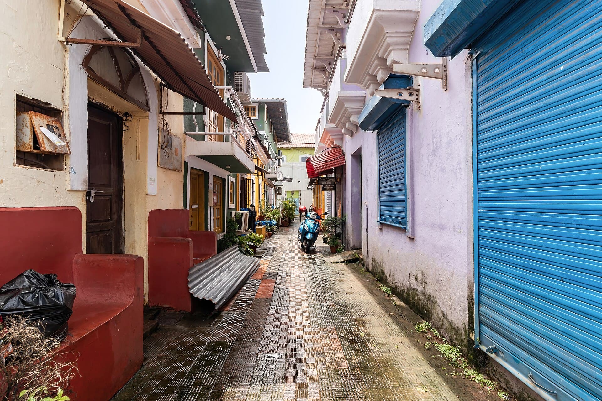 A narrow paved lane in Fontainhas, Panaji, lined by heritage houses with a bright blue shuttered shopfront and a scooter parked mid-lane