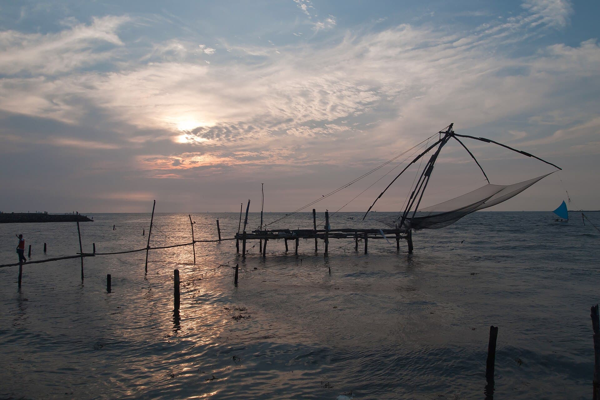 A shore-operated Chinese fishing net silhouetted over the water at Fort Kochi as the sun sets behind clouds