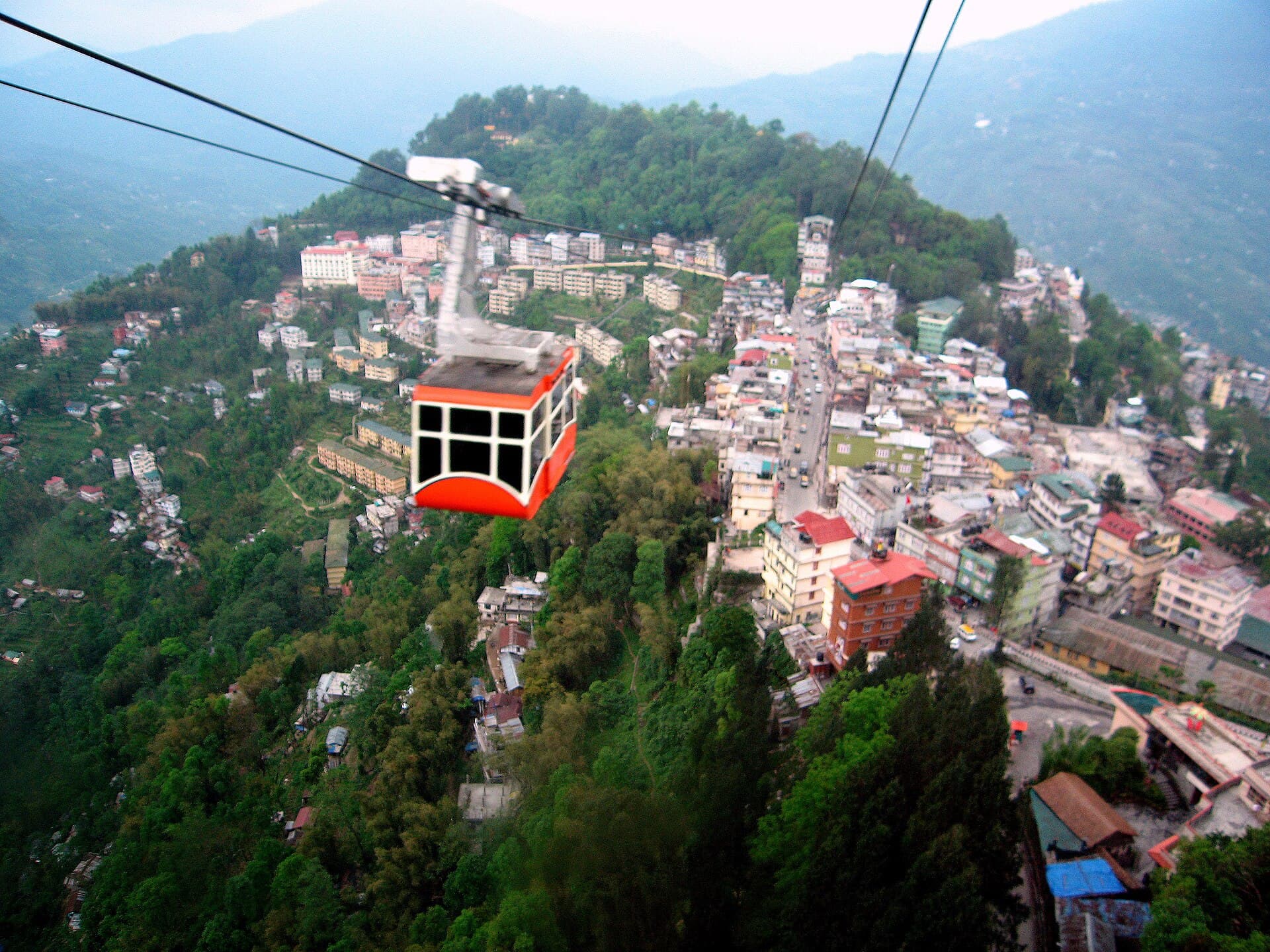 A red Gangtok Ropeway cabin suspended high above the hill town's stacked houses and winding main road