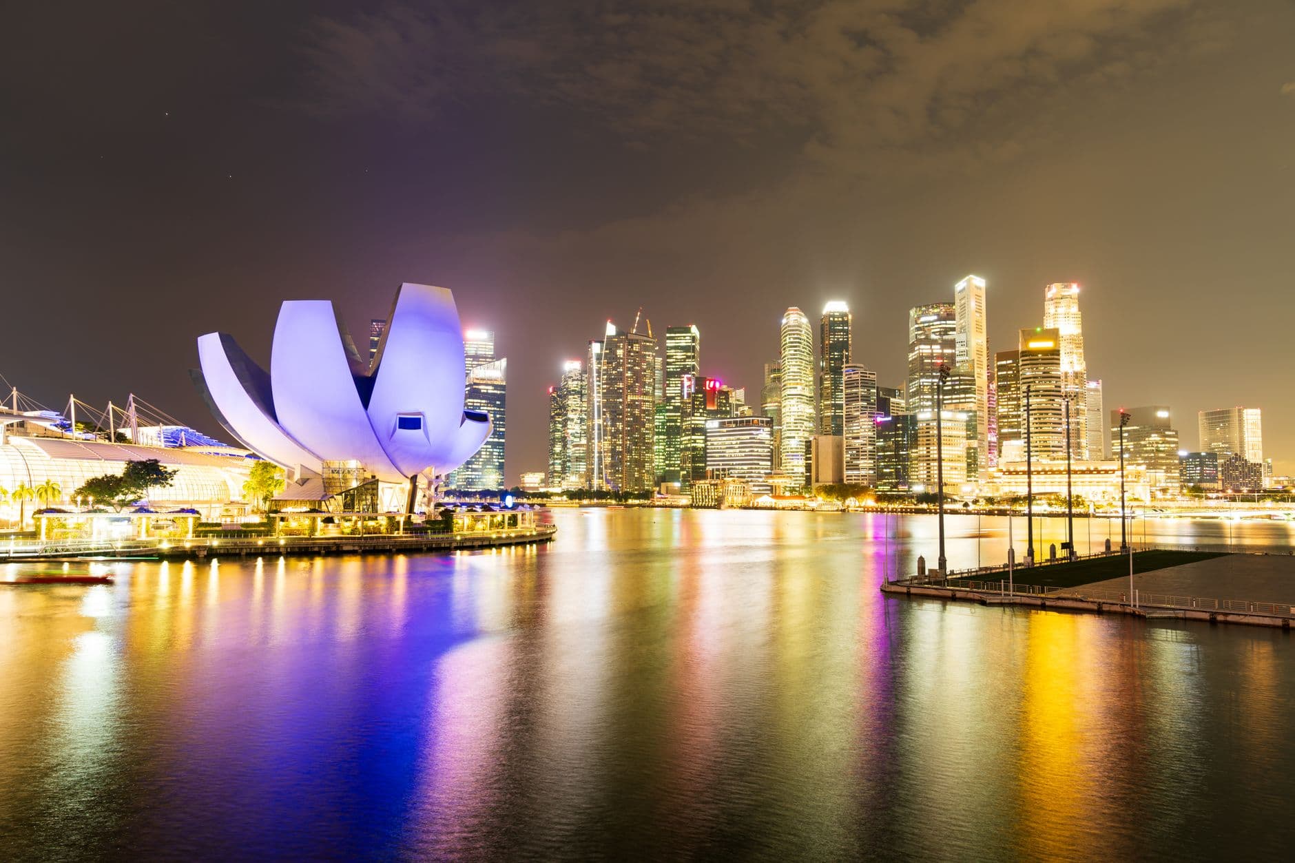 Marina Bay illuminated at night, the ArtScience Museum's lotus-shaped roof and the CBD skyline reflected in the water