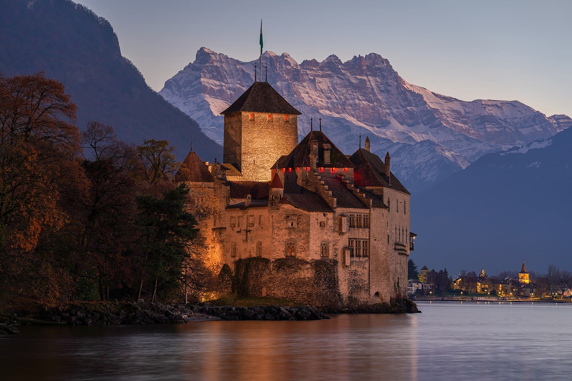 Chillon Castle glowing at dusk on the shore of Lake Geneva, the snow-capped Dents du Midi rising behind