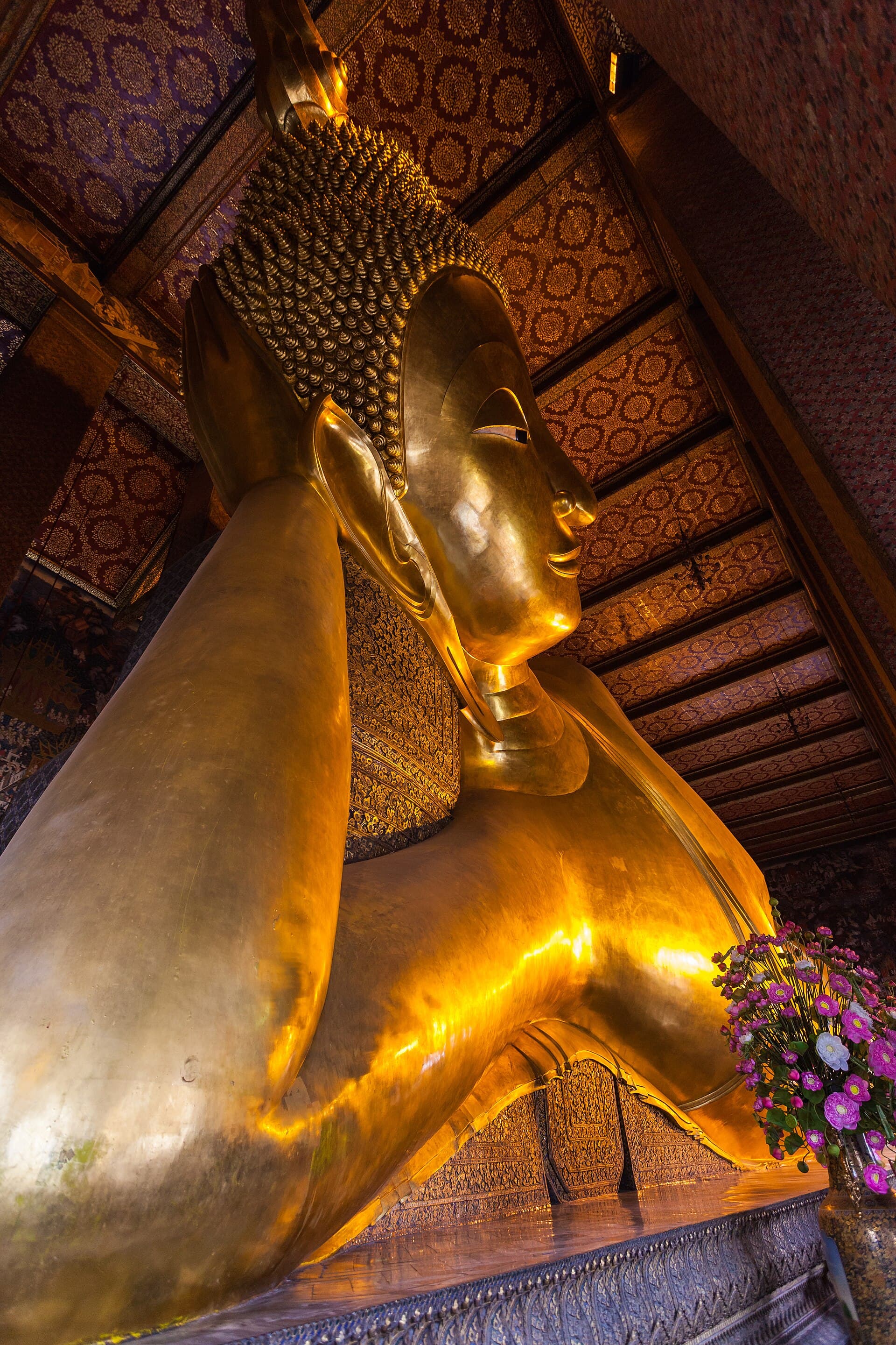Close-up of the gold-plated Reclining Buddha's face and shoulder at Wat Pho, patterned temple ceiling above